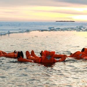 Un voyage de groupe WeRoad en combinaisons d'immersion oranges flottant sur le dos dans l'eau glacée au coucher du soleil.