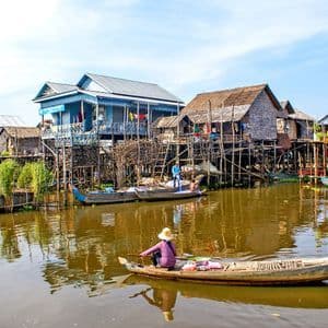 A person in a small boat paddles through a village of colorful houses built on stilts over the water.