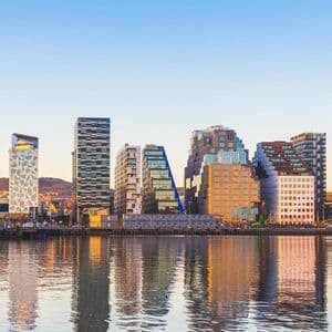 Uno skyline moderno di città con stili architettonici vari riflessi in acque calme sotto un cielo azzurro e limpido.