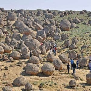 Eine WeRoad-Gruppenreise wandert auf einem Pfad durch eine hügelige Landschaft mit großen, kugelförmigen Felsformationen unter klarem Himmel.