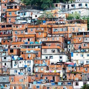 Fitte costruzioni in mattoni rossi e bianchi di una favela che ricoprono una collina verde.