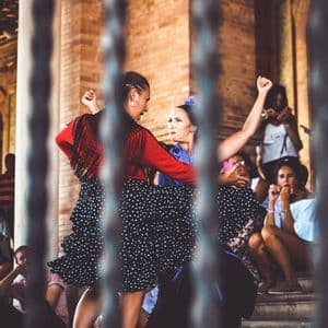 Flamencotänzer in traditionellen Kleidern treten auf einem Steinplatz vor einem auf Stufen sitzenden Publikum auf.