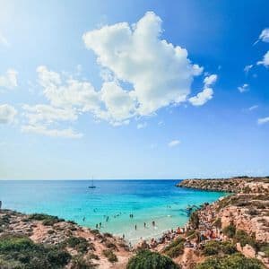 Una veduta dall'alto di una cala con acqua turchese splendente, delimitata da scogliere rocciose dove le persone nuotano e prendono il sole.