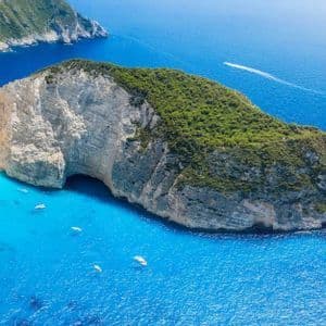Vista aerea di un naufragio su una spiaggia isolata di sabbia bianca in una cala, circondata da scogliere e acqua turchese con barche.