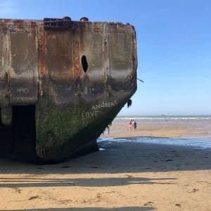 Un grande blocco di cemento consumato da un naufragio giace su una spiaggia sabbiosa, con una persona che sbircia dalla cima.