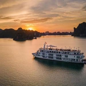 Un paquebot blanc flotte sur une eau calme, entouré d'îles rocheuses au coucher du soleil.