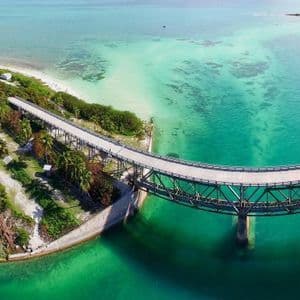 Una vista aerea di un lungo ponte curvo che si estende da una penisola verde su acque oceaniche limpide e turchesi.