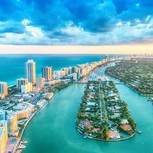 Vista aerea di una città costiera con grattacieli lungo la spiaggia e un corso d'acqua che separa isole residenziali.