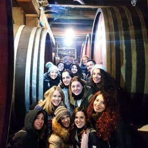 Eine WeRoad-Gruppe lachender Menschen, die für ein Foto in einem engen Weinkeller zwischen großen Holzfässern posieren.