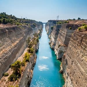 Un canal largo y estrecho con agua turquesa fluye entre empinados acantilados de roca estratificados en un día soleado.