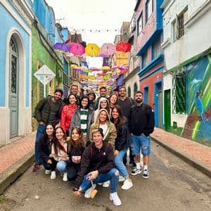 Un viaje en grupo de WeRoad posa para una foto en una calle colorida bajo un dosel de paraguas colgantes.