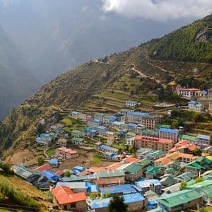 Una vista aérea de un pueblo con tejados coloridos azules, verdes y rojos, construido en las laderas aterrazadas de una montaña empinada.