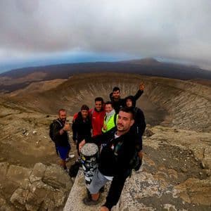 Un viaggio di gruppo WeRoad scatta un selfie sull'orlo di un cratere vulcanico sotto un cielo nuvoloso.