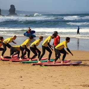 Un viaggio di gruppo WeRoad partecipa a una lezione di surf, imparando a stare in piedi sulle tavole da surf su una spiaggia sabbiosa.