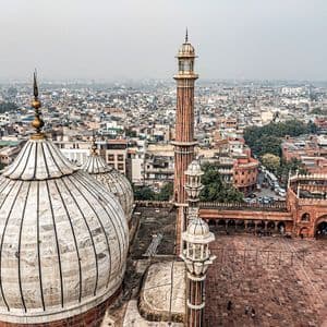 Vista aérea de las cúpulas blancas y el alto minarete de una mezquita sobre un extenso y brumoso paisaje urbano.