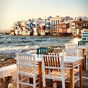 Tavoli e sedie bianchi su un patio in pietra si affacciano sulle onde che si infrangono sulla costa di una città costiera.