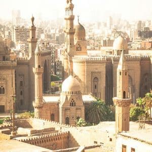 Un complesso storico di moschee in pietra con cupole e minareti che domina un paesaggio urbano denso sotto un cielo luminoso e velato.