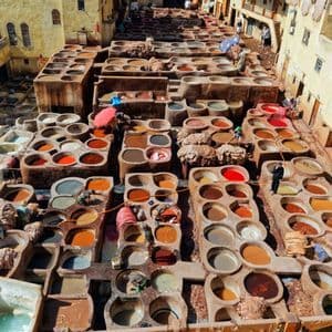 Eine Luftaufnahme einer traditionellen Gerberei mit zahlreichen Steinbottichen, gefüllt mit bunten Farbstoffen, in denen Menschen arbeiten.