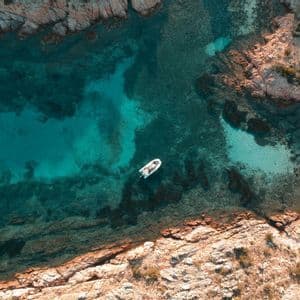 Veduta aerea di una barca bianca che galleggia su acque limpide turchesi in una cala rocciosa.