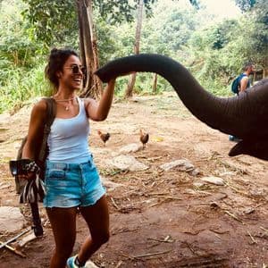 Une femme souriante, lors d'un voyage de groupe WeRoad, touche la trompe d'un éléphant dans une clairière de jungle.