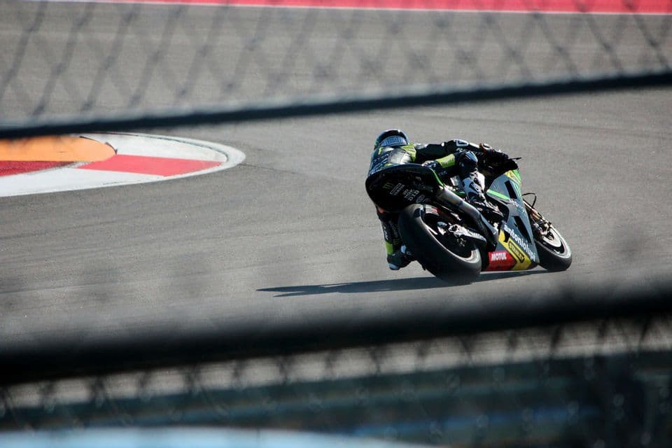 Un motociclista si piega con un'inclinazione estrema in curva su una pista asfaltata sotto il sole splendente.