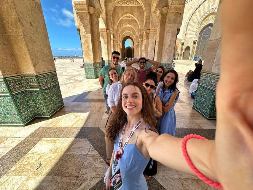 Eine WeRoad-Gruppe lächelt und posiert für ein Selfie, während sie unter einer verzierten Bogenkolonnade in einer Reihe steht.