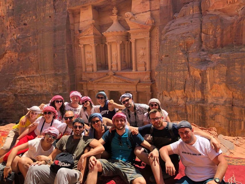 Un viaje en grupo de WeRoad posa para una foto en una alfombra roja frente a un antiguo templo tallado en un acantilado rocoso.