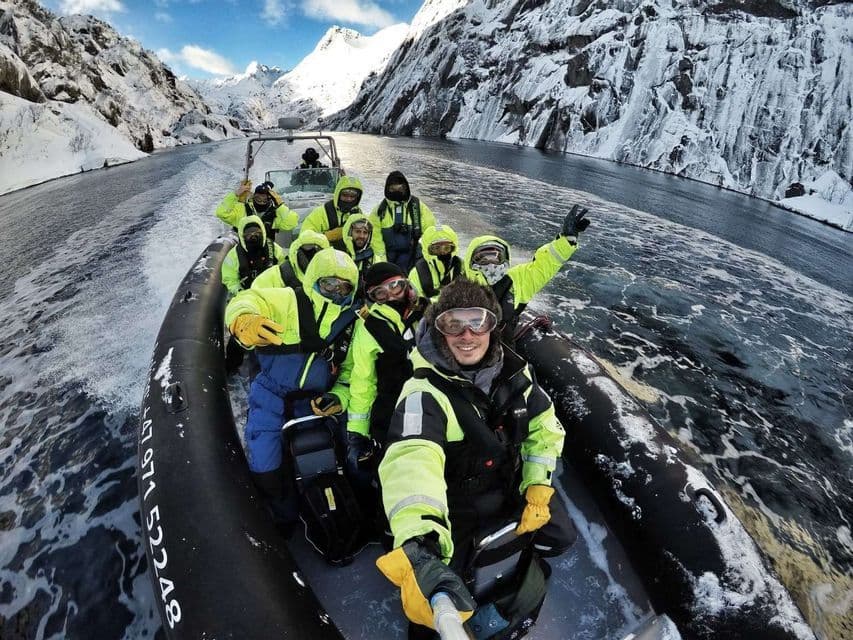 Un gruppo WeRoad con abbigliamento invernale vivace si scatta un selfie su una barca, navigando un fiordo tra montagne innevate.