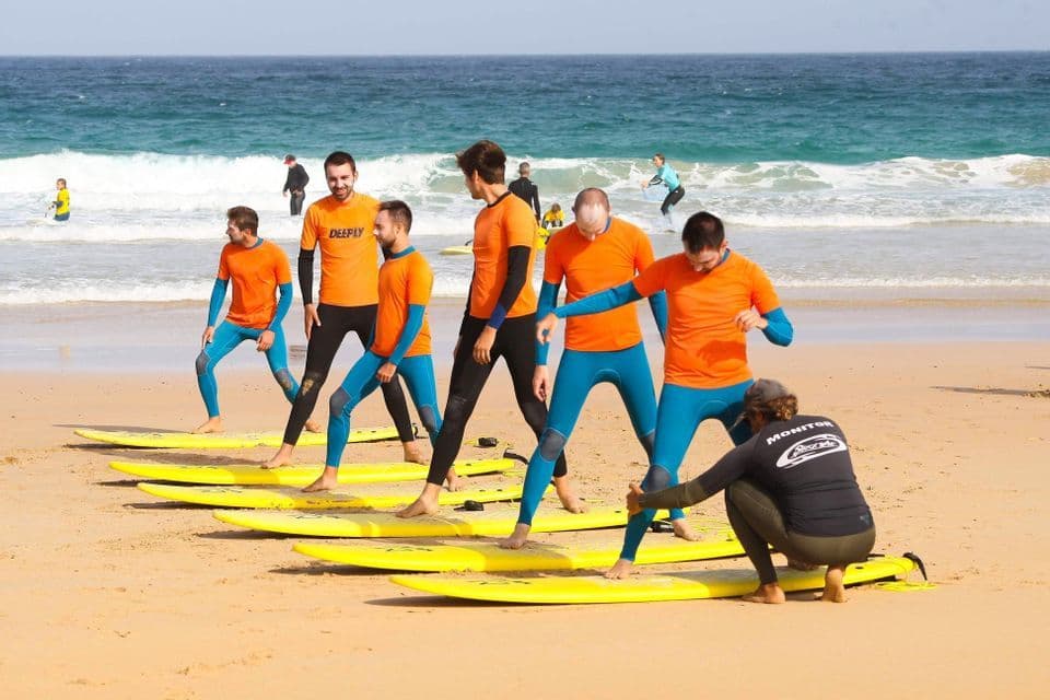 Un gruppo WeRoad partecipa a una lezione di surf, imparando a stare in piedi su tavole da surf gialle su una spiaggia di sabbia.