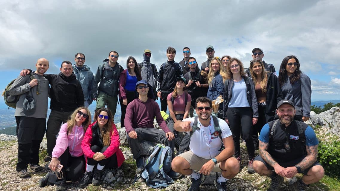 A WeRoad group trip poses for a group photo on a rocky mountaintop under a cloudy sky.