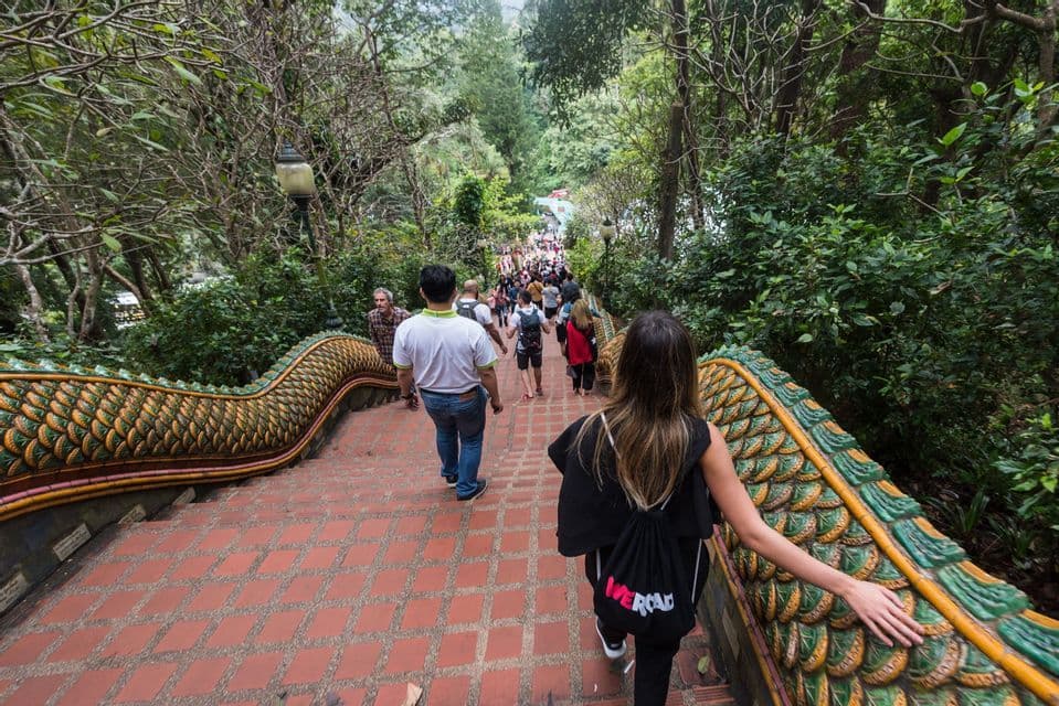 Un viaggio di gruppo WeRoad scende una lunga scalinata piastrellata con balaustre di drago ornate, circondata da una lussureggiante foresta verde.