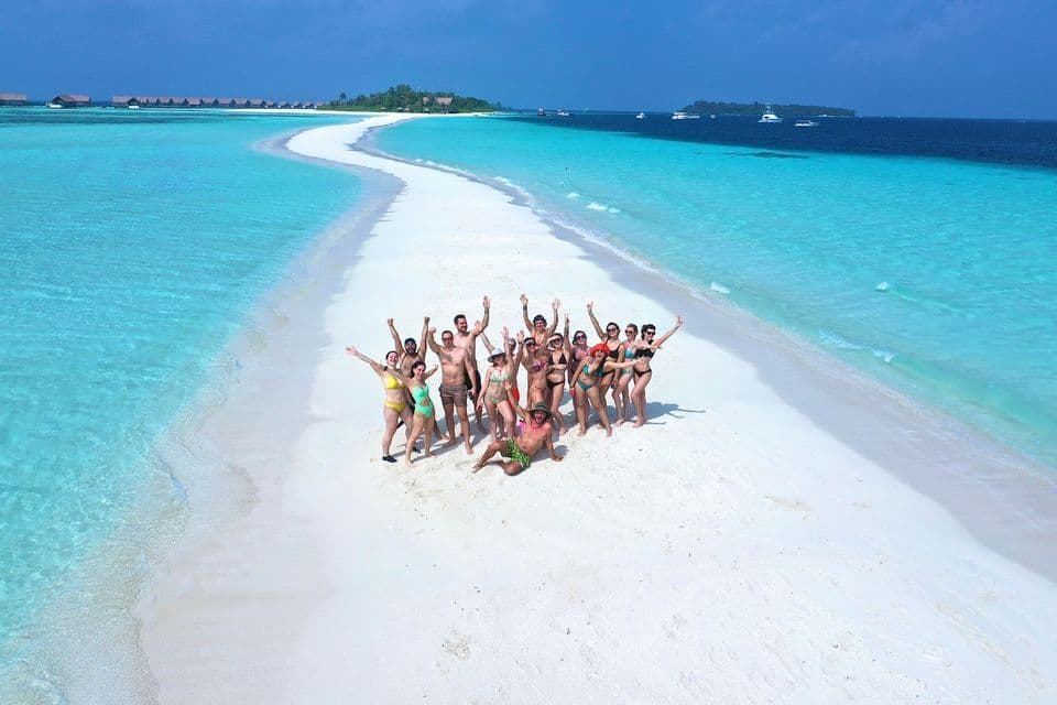 An aerial view of a WeRoad group trip posing on a white sandbar that stretches through turquoise ocean water.
