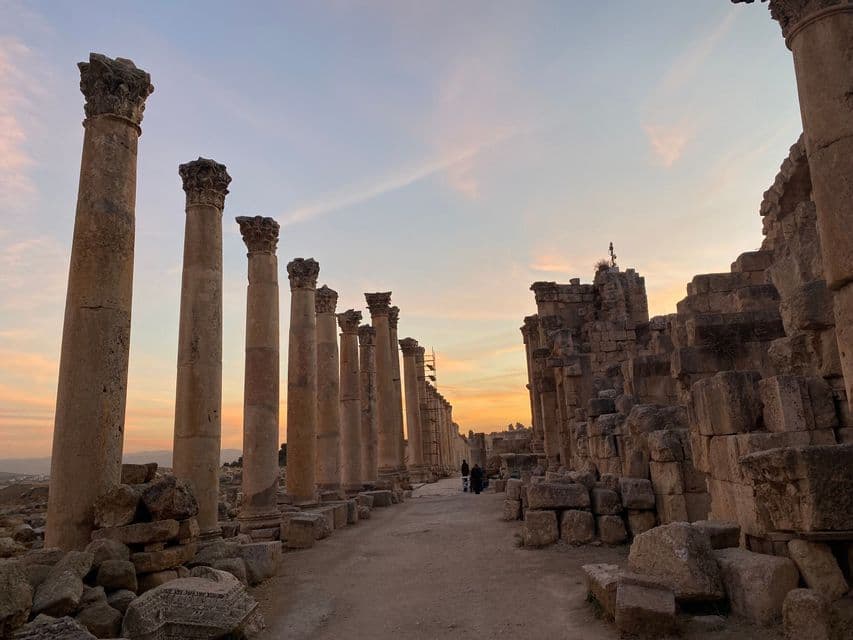 Una hilera de antiguas columnas corintias flanquea un sendero a través de ruinas arqueológicas bajo un cielo al atardecer.