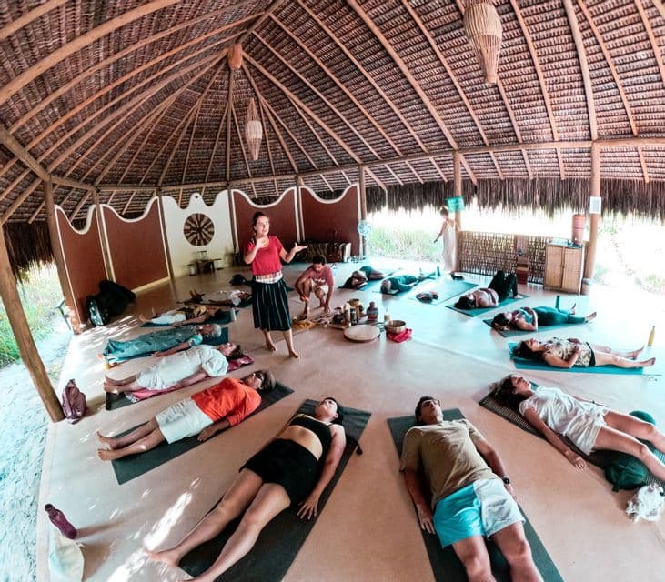 Un gruppo WeRoad è disteso su tappetini da yoga in cerchio durante una lezione di meditazione guidata all'interno di una capanna rotonda con tetto di paglia.