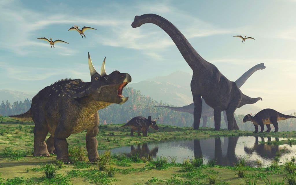 Un triceratops rugiente se alza cerca de un abrevadero con branquiosaurios y otros dinosaurios en un exuberante valle prehistórico.