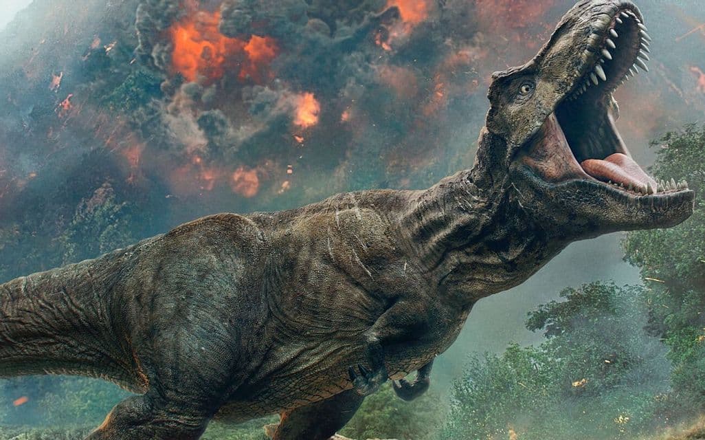 Un Tiranosaurio Rex ruge con la boca abierta mientras una explosión de fuego se eleva en el fondo sobre un bosque exuberante.