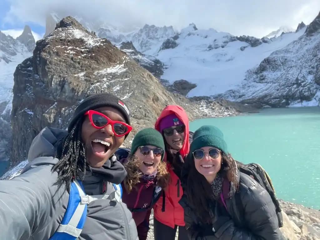 A smiling WeRoad group taking a selfie in front of a glacial lake and snowy mountains.