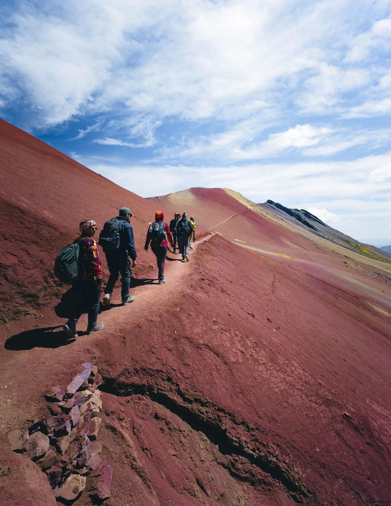 Un grupo de WeRoad camina por un sendero de montaña de tierra roja bajo un cielo con nubes.