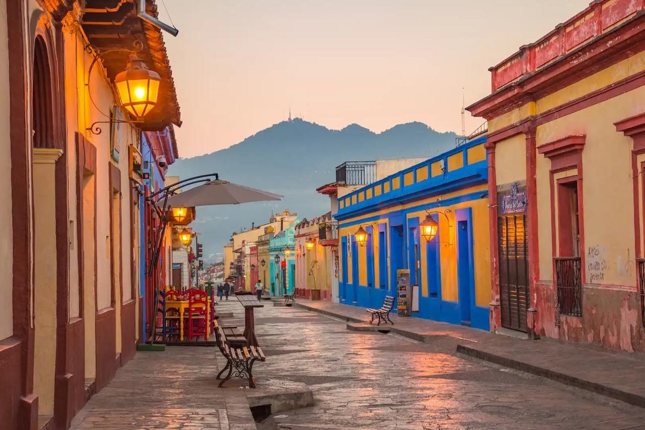 Strada coloniale di San Cristóbal de las Casas al tramonto con facciate colorate, lampioni dorati e montagna sullo sfondo, Chiapas, Messico