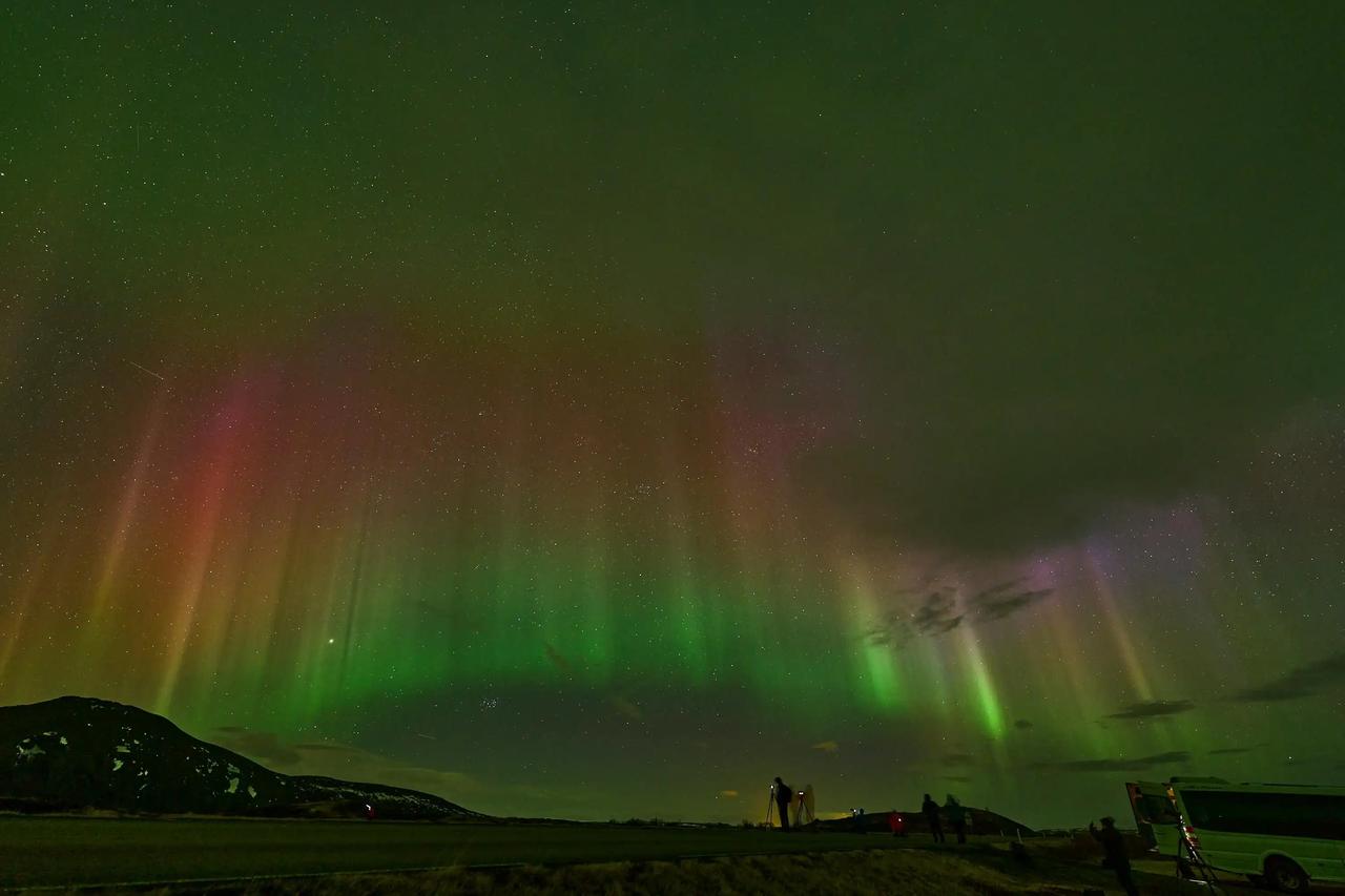 Un viaggio di gruppo WeRoad ammira e fotografa le colorate Aurore Boreali nel cielo notturno stellato.