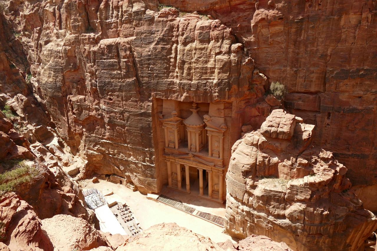 Un templo ornamentado con columnas talladas en un acantilado de roca roja, visto desde un punto elevado.