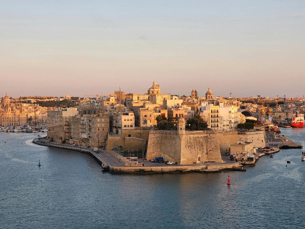Une ville fortifiée historique sur une presqu'île entourée d'eau, avec ses bâtiments en pierre éclairés par le soleil couchant.