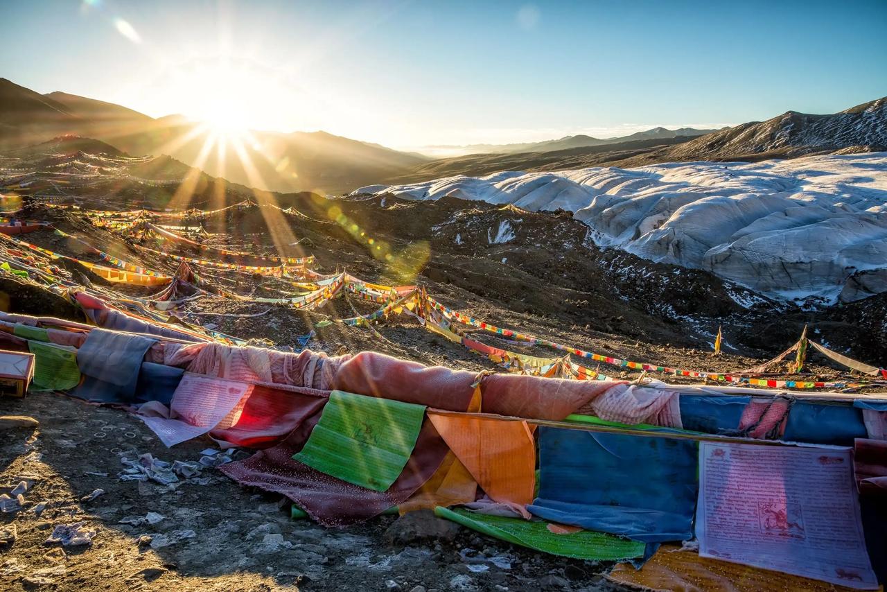 Banderas de oración de colores en un paso de montaña con el sol saliendo entre las cumbres.