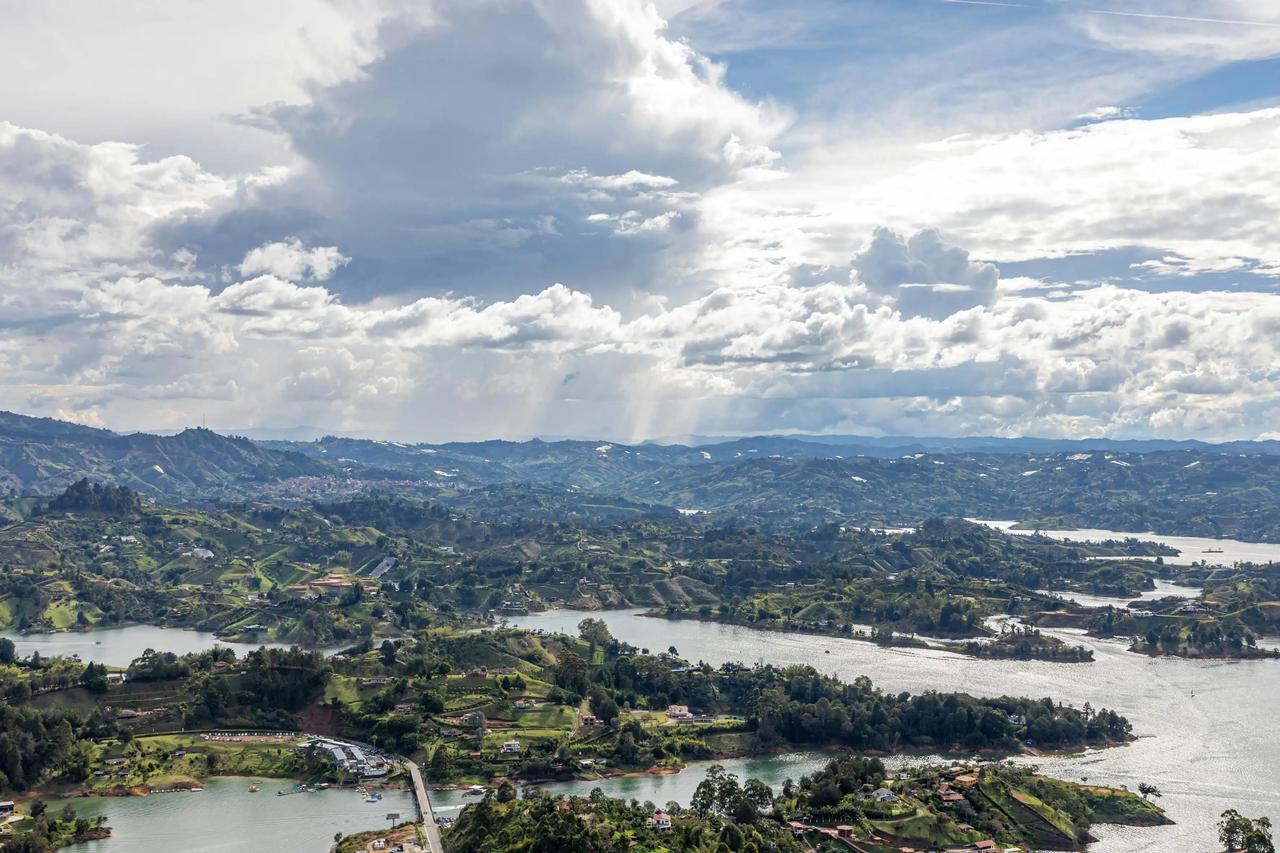 Una vista aérea de un gran embalse serpenteando a través de verdes colinas onduladas bajo un cielo dramático y nublado.