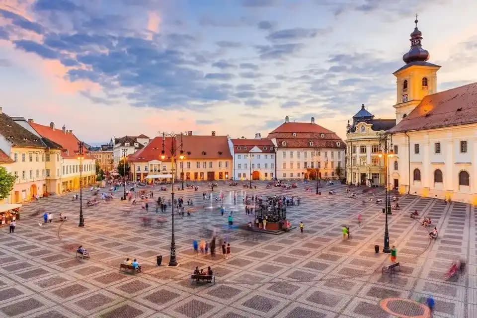 Una vista elevada de una bulliciosa plaza europea con adoquines estampados y edificios históricos al atardecer.