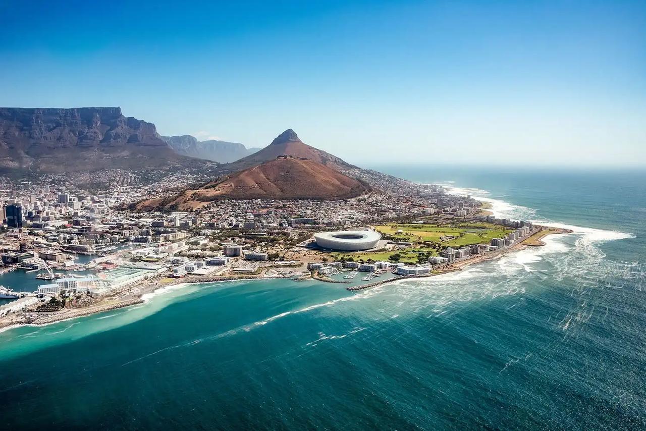 Luftaufnahme von Kapstadt mit dem Tafelberg im Hintergrund, dem Signal Hill, dem Kapstadt-Stadion und der türkisfarbenen Küste des Atlantischen Ozeans