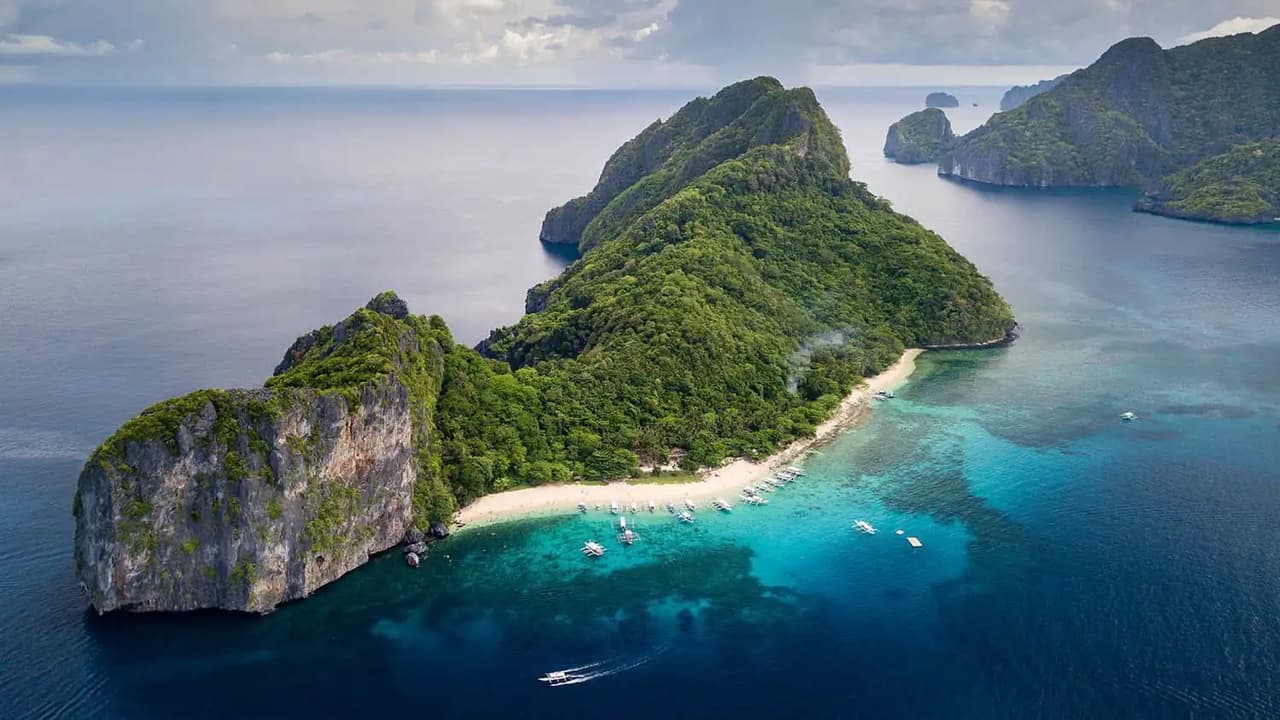 Vista aérea de una isla con acantilados, vegetación y playa de arena blanca en un mar turquesa.