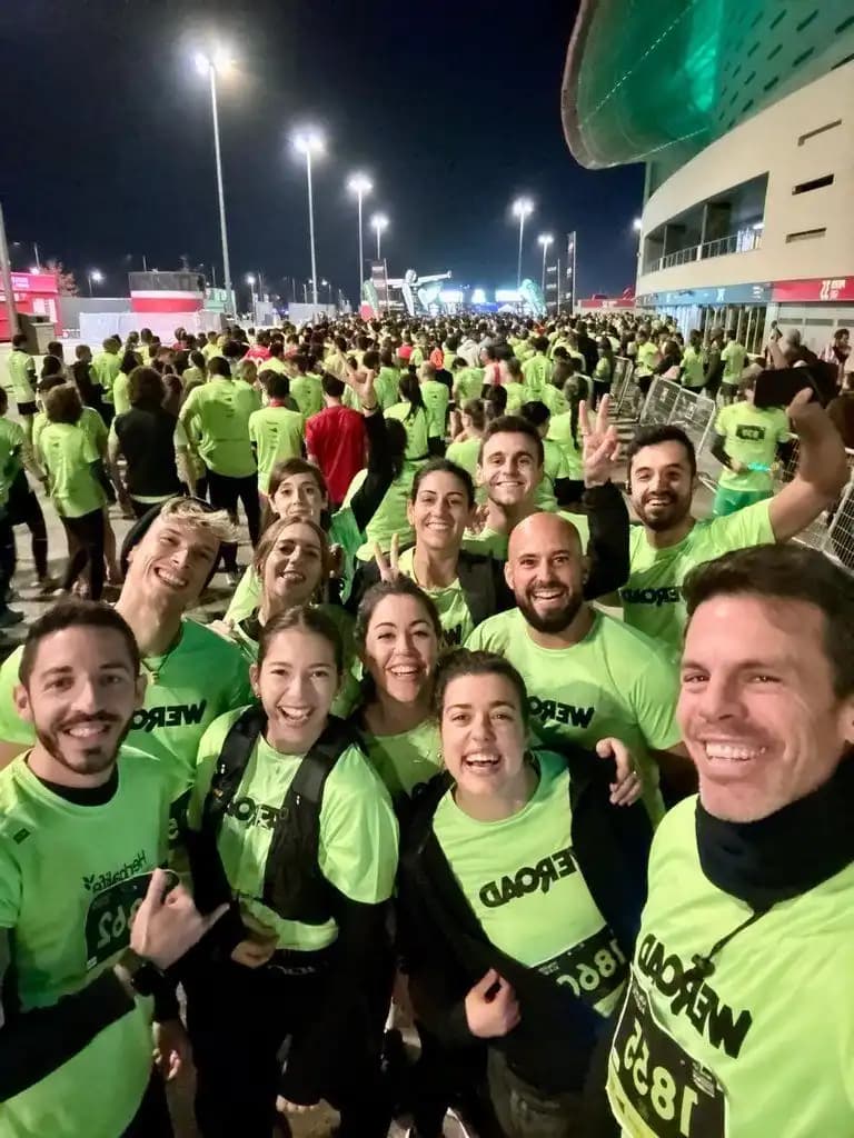 Una grande folla con magliette WeRoad verdi e pettorali, riunita di notte fuori da uno stadio prima di una corsa.