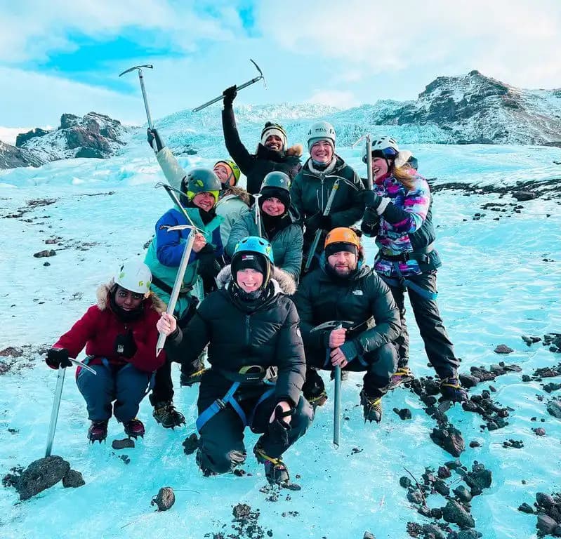 Un viaje en grupo de WeRoad con ropa de invierno posando con cascos y piolets en un glaciar entre picos nevados.