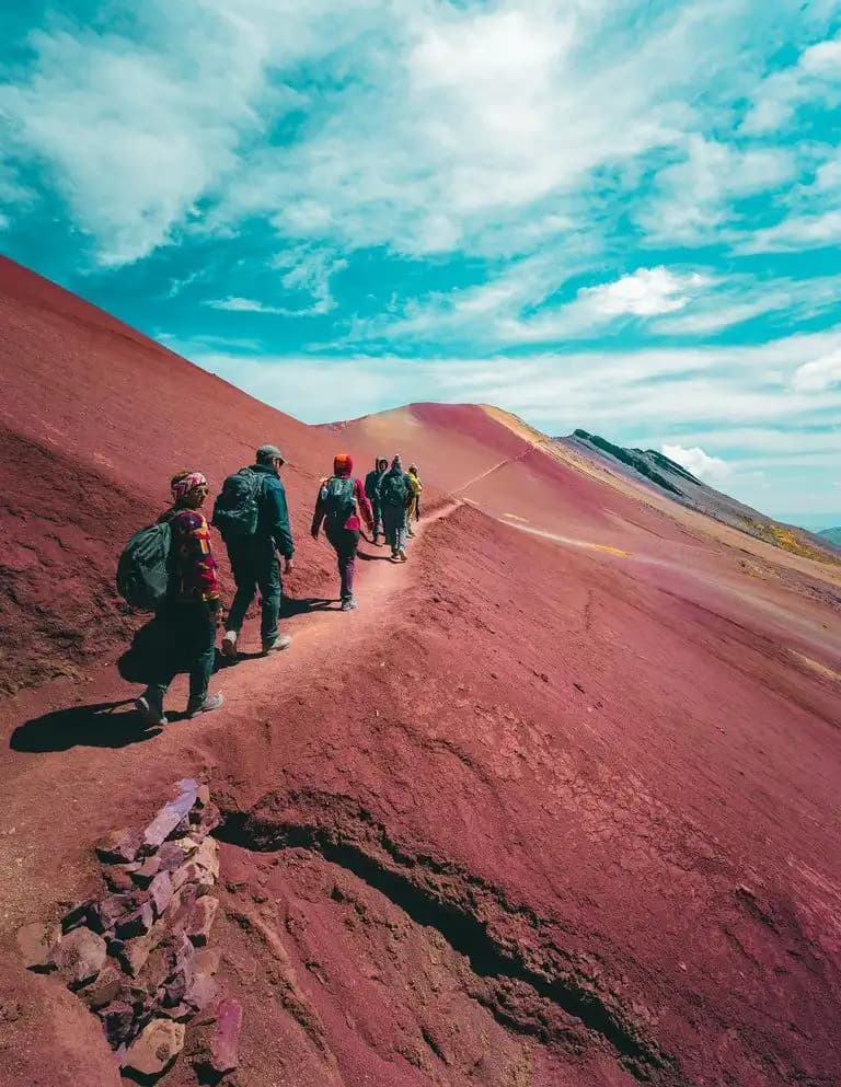 Un viaggio di gruppo WeRoad in trekking su un crinale di montagna rossa con zaini, sotto un cielo nuvoloso.